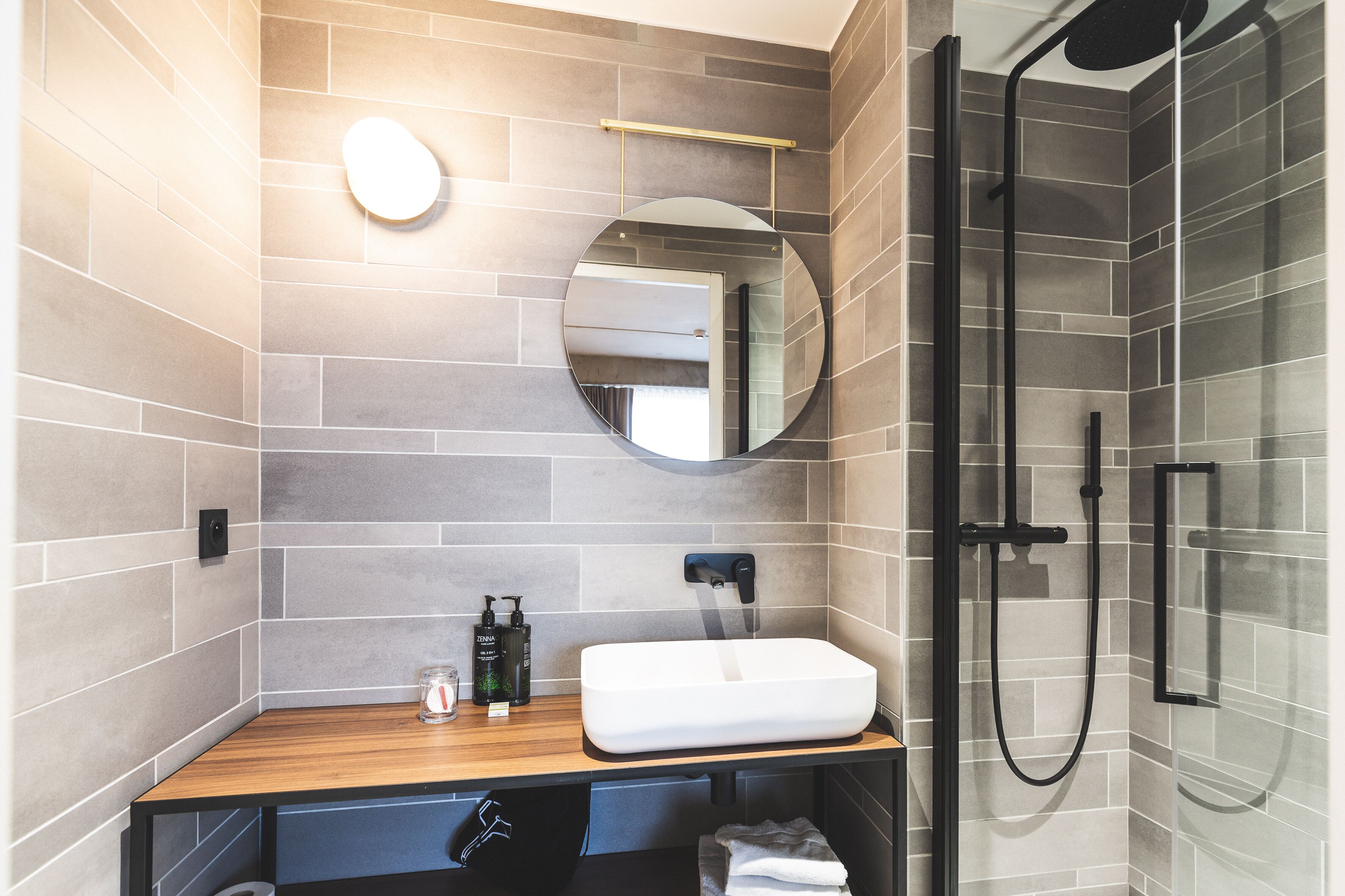 A modern bathroom with a wooden vanity, a round mirror, a white sink, and a glass shower enclosure.