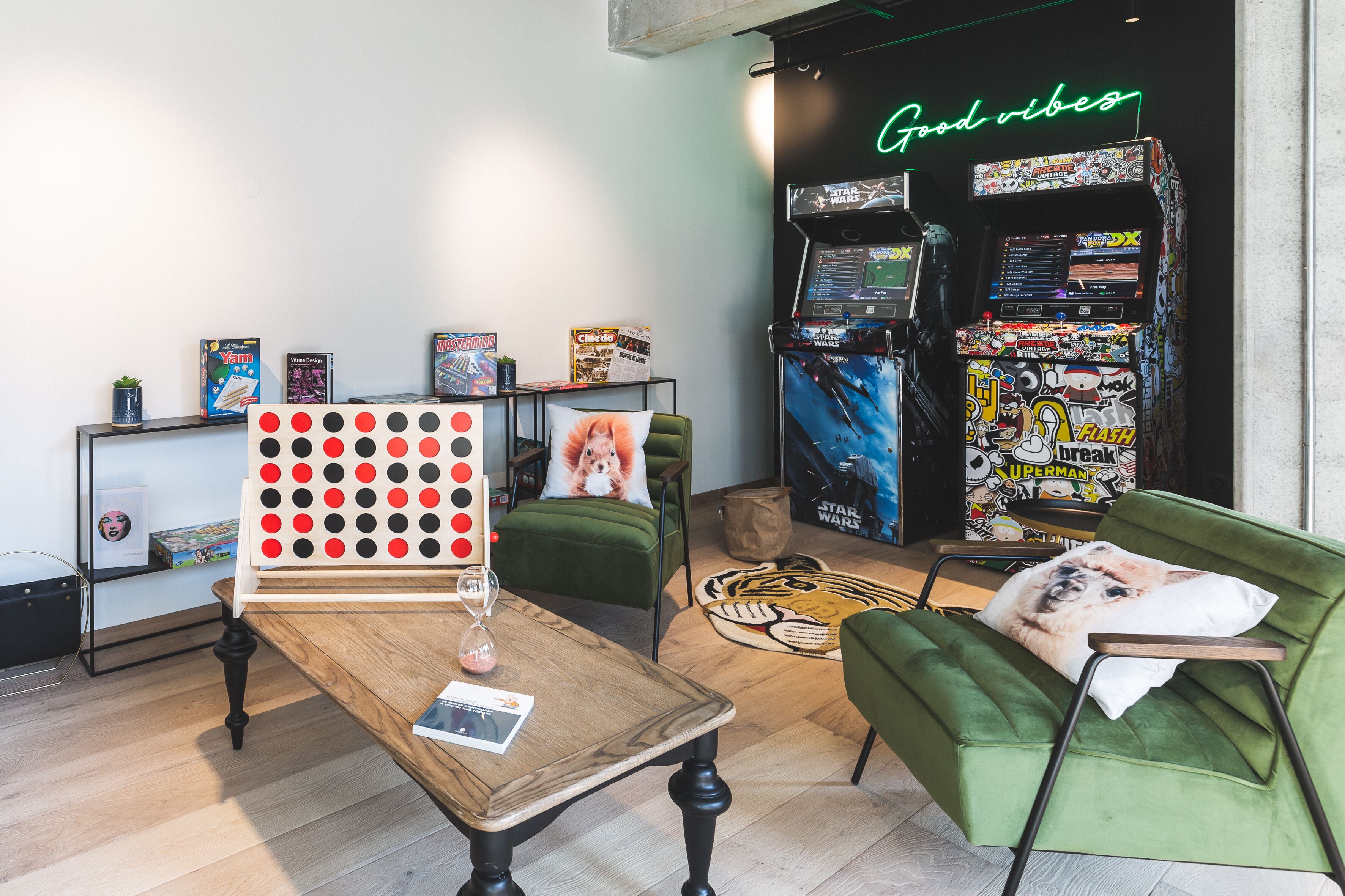 A room with a wooden table, green chairs, a neon sign, and a Star Wars arcade machine.