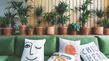Un sofá verde con almohadones decorativos y una fila de macetas contra una pared de madera.