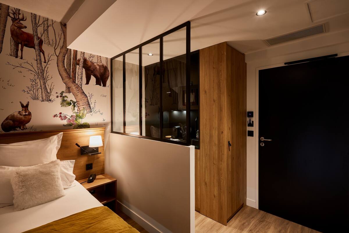 A bedroom with a bed, nightstand, lamp, and a wall mural.