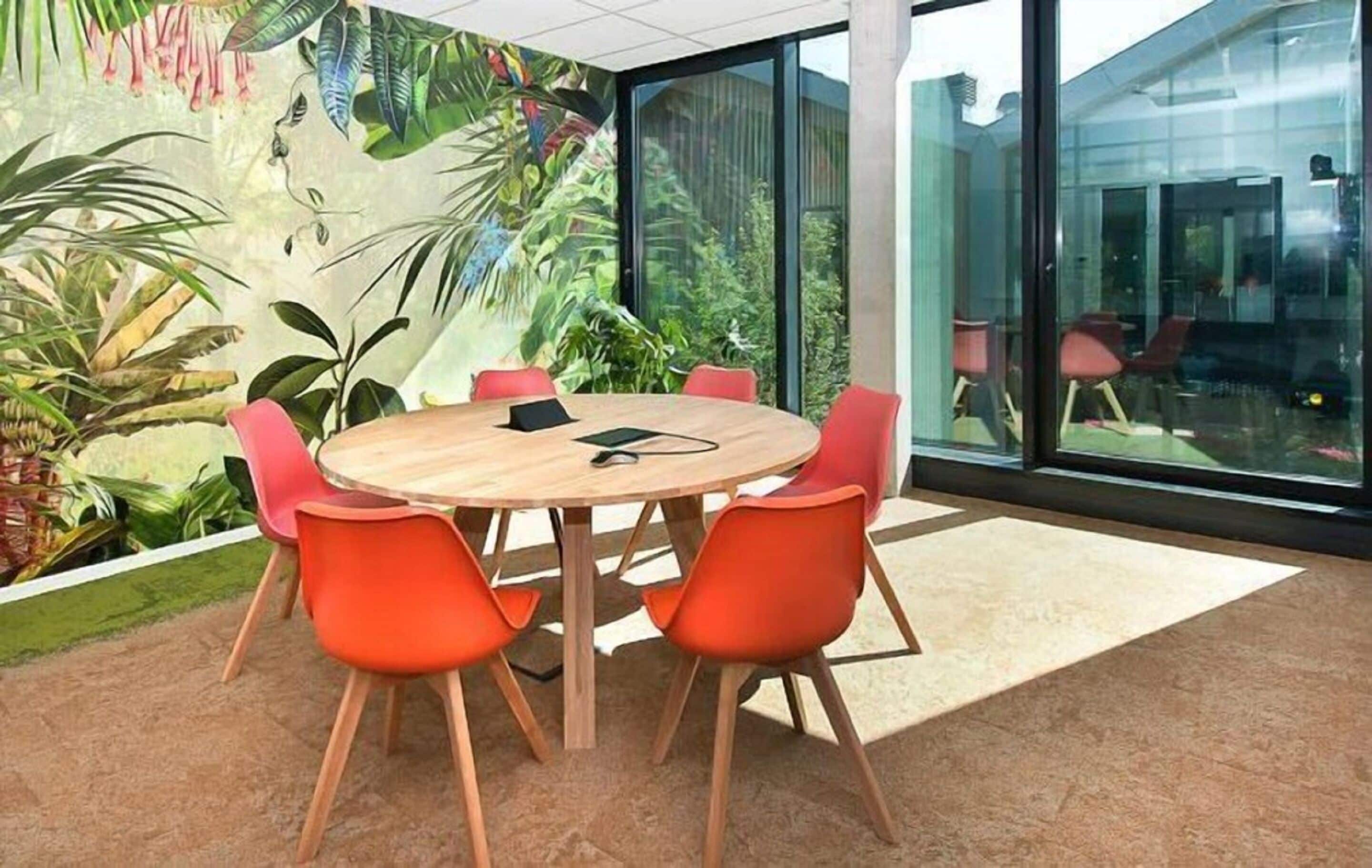 Un salón de conferencias con una mesa redonda, seis sillas anaranjadas y un mural de plantas tropicales en la pared.