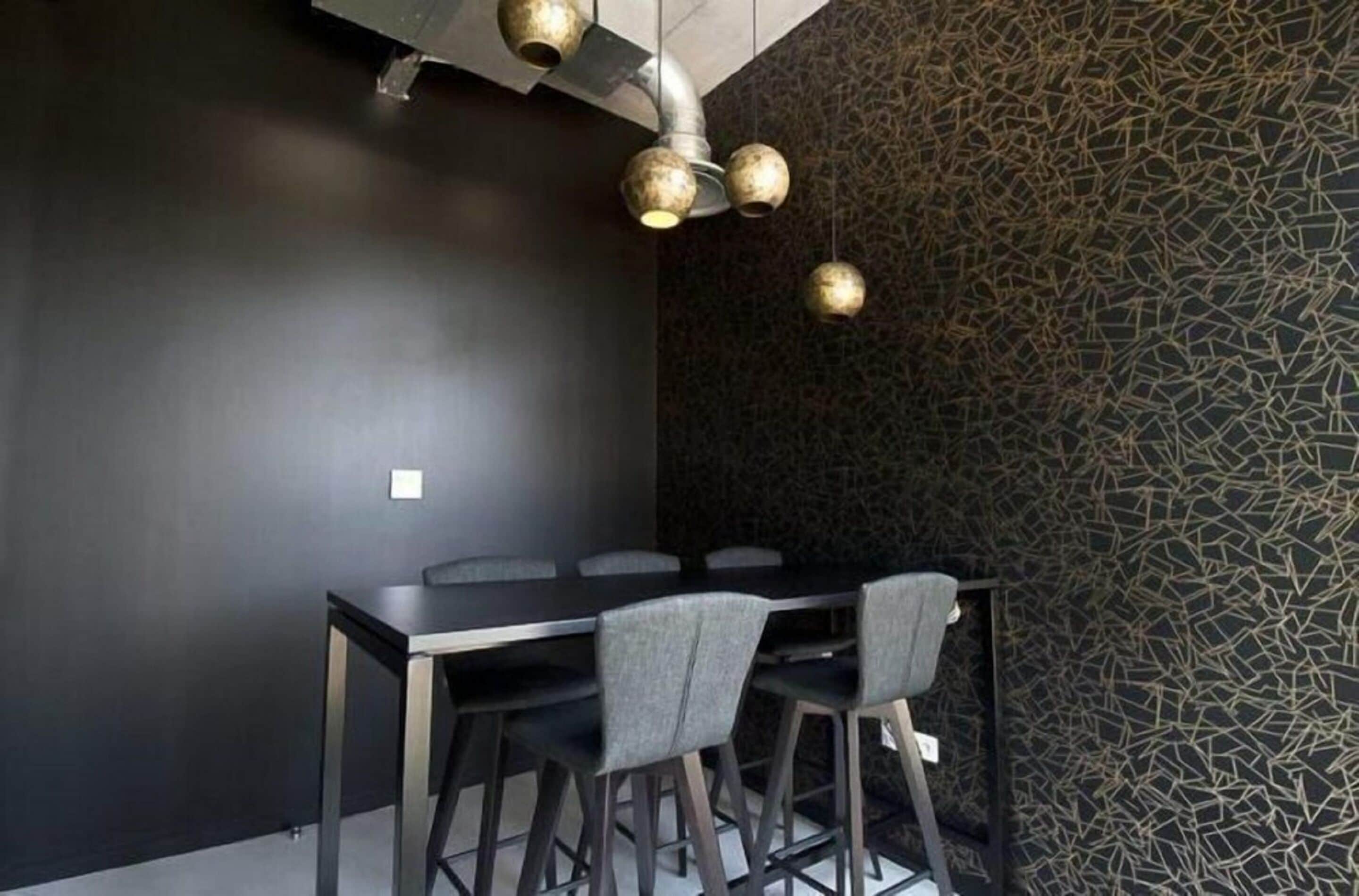 A modern dining area with a dark wall, a patterned wall, and a black table with chairs.
