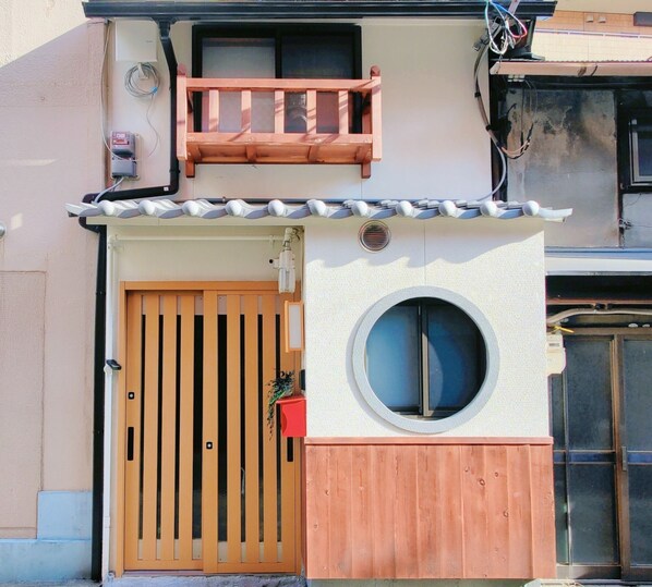 A traditional Japanese house with a wooden gate, a small balcony, and a circular window.