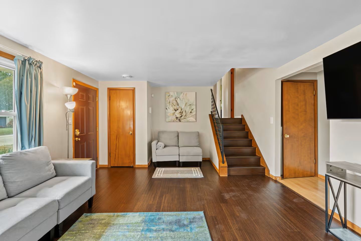 Un vaste espace de vie comprenant un canapé, un tapis, un escalier et un téléviseur à écran plat.