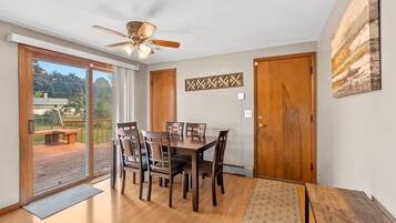 A dining area with a table and chairs, a ceiling fan, and a view through a glass door to an outdoor deck.