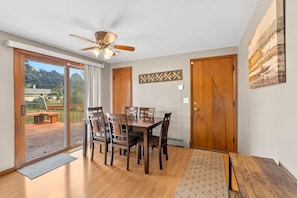 A dining area with a table and chairs, a ceiling fan, and a view through a glass door to an outdoor deck.