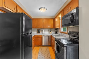 A compact kitchen with wooden cabinets, a black refrigerator, a microwave, a stove, and a dishwasher.
