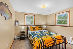 A hotel room with a bed, two bedside tables, a nightstand, a window with blinds, and a ceiling light.