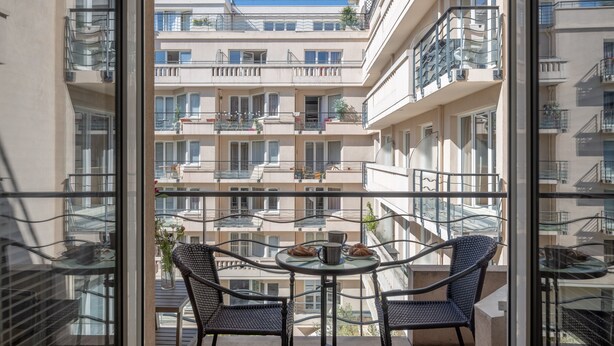 Un balcón con dos sillas y una mesa, con vista a un edificio de varios pisos y balcones.