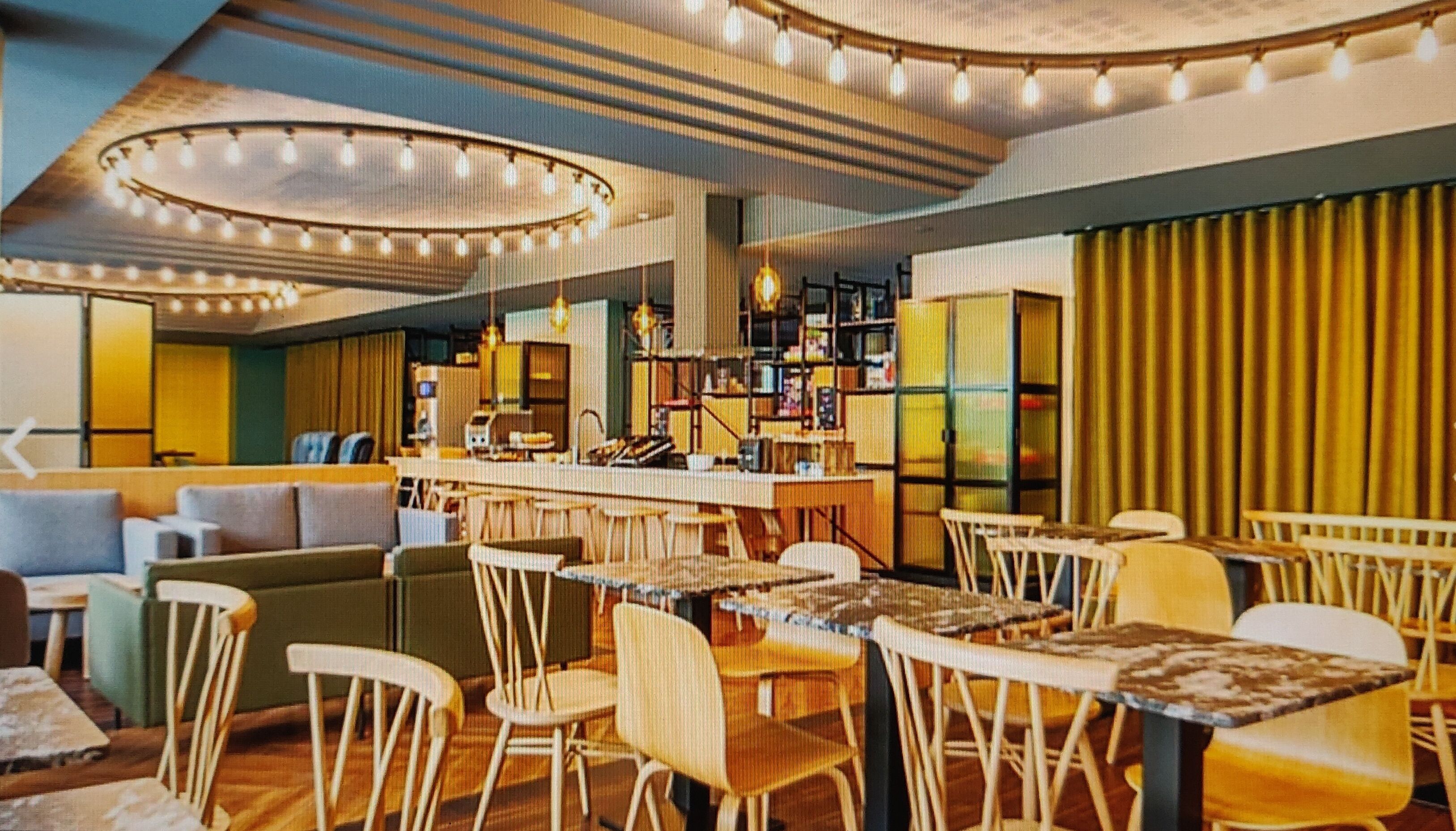 Ein modernes Restaurant mit Barbereich, Holzhockern und einer Mischung aus Sitzgelegenheiten, darunter Sofas und Tische.