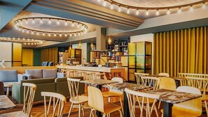 Un restaurante moderno con zona de bar, sillas de madera y una variedad de opciones de asientos, incluyendo sofás y mesas.