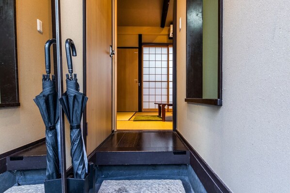 A traditional Japanese interior with a wooden door, tatami mat flooring, and black umbrellas leaning against the wall.