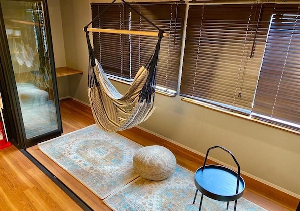 A room with a hammock chair, a round ottoman, and a blue chair.