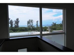A room with a large window overlooking a coastal area, including trees and a view of the sea.