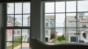Une vue depuis une fenêtre, avec une chaise blanche au premier plan, donnant sur un quartier résidentiel avec des maisons et une plage.
