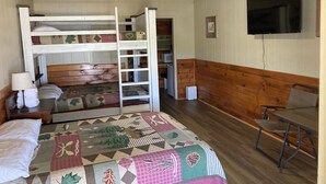 A room with bunk beds, a ceiling fan, a TV, and a wooden bench. - Lake front Cabin #11 with Porch - Cabin with kitchen, steps from Possum Kingdom Lake (Graham)