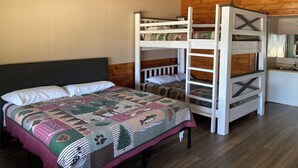 A bunk bed room with a quilted bedspread, a ceiling fan, and wooden walls. - Lake front Cabin #11 with Porch - Cabin with kitchen, steps from Possum Kingdom Lake (Graham)