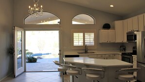 A modern kitchen with white cabinets, a large island with bar stools, a chandelier, and a view through the glass door. - South Mountain Sanctuary-backyard privacy- -cul-de-sac- pool-STR2024003324 (Phoenix)