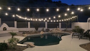 A pool area with string lights, a fountain, and a seating area with chairs. - South Mountain Sanctuary-backyard privacy- -cul-de-sac- pool-STR2024003324 (Phoenix)