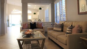 A spacious living room with a sofa, coffee table, and a dining area in the background. - South Mountain Sanctuary-backyard privacy- -cul-de-sac- pool-STR2024003324 (Phoenix)