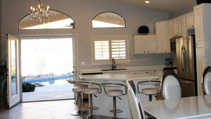 A modern kitchen with white cabinets, a stainless steel refrigerator, and a bar area with stools. - South Mountain Sanctuary-backyard privacy- -cul-de-sac- pool-STR2024003324 (Phoenix)