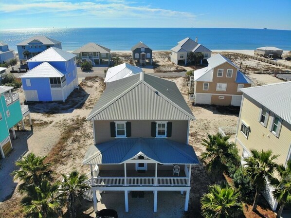 A beachfront property with multiple houses, a prominent house with a balcony in the foreground, and a sandy beach in the background.