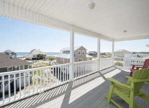 A covered porch with white railings, a view of the beach, and a few houses in the background.