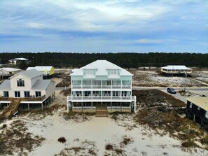 A coastal house with a balcony, a staircase, and a sandy beach in the foreground. - Beachfront and Updated! Pets OK! (Gulf Shores)