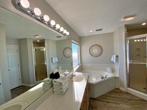 A bathroom with two sinks, a large mirror with lights, a shower, and a door leading to another room. - Beachfront and Updated! Pets OK! (Gulf Shores)