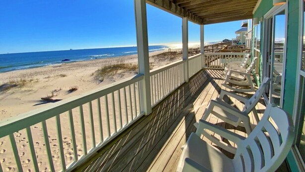 Een balkon aan het strand met uitzicht op de oceaan, een houten terras en strandstoelen.