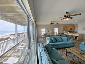 A spacious living area with a large blue sofa, a wooden coffee table, and a view of the beach through large windows. - Beachfront and Updated! Pets OK! (Gulf Shores)