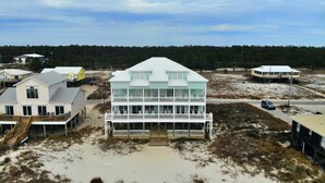 Een huis aan zee met balkon, trap en een zandstrand op de voorgrond.