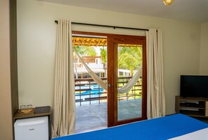 Habitación de hotel con cama, televisión, refrigerador pequeño y vista a una piscina y palmeras.