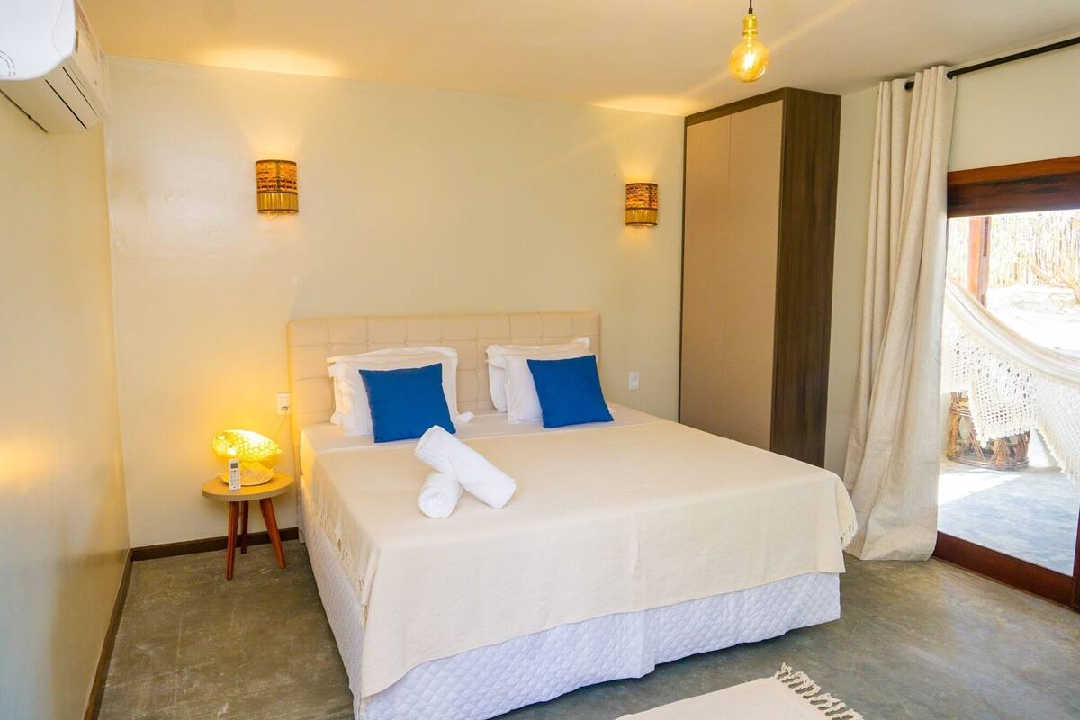 A hotel room with a bed, bedside lamps, a small table, and a view of the outdoors.