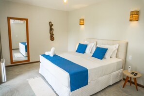Una habitación de hotel con una cama grande, una mesita de noche, un espejo y dos lámparas fijadas a la pared.