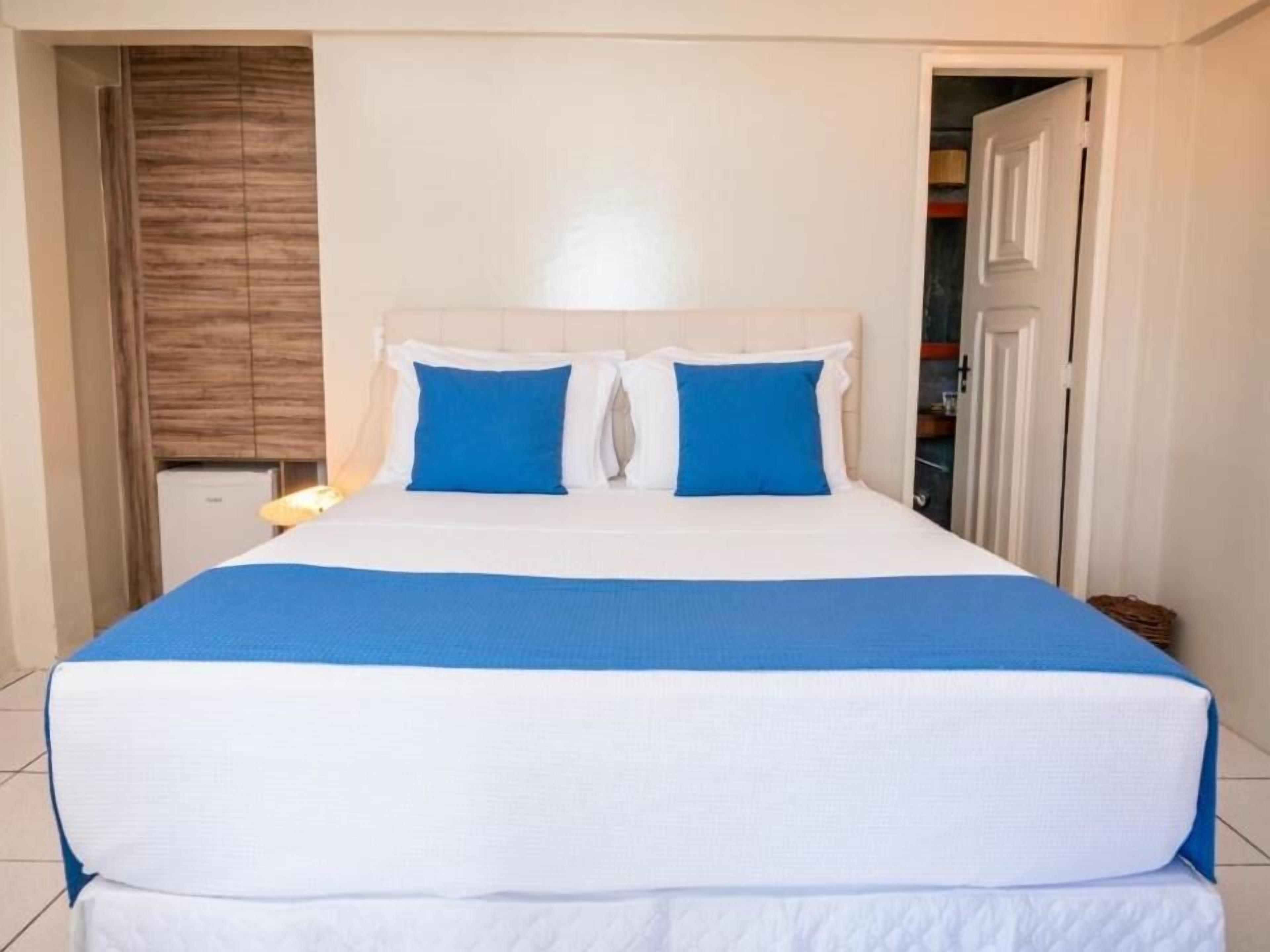 A neatly made bed with white and blue bedding, a wooden wardrobe, and a white door in the background.