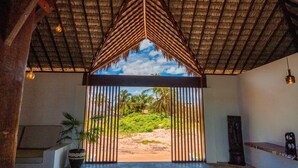 Una habitación con techo de paja, vista a una playa y una planta en maceta.
