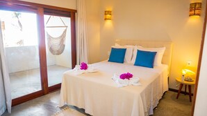 Habitación de hotel con cama, dos apliques, una mesita de noche con lámpara y vistas a través de un ventanal.