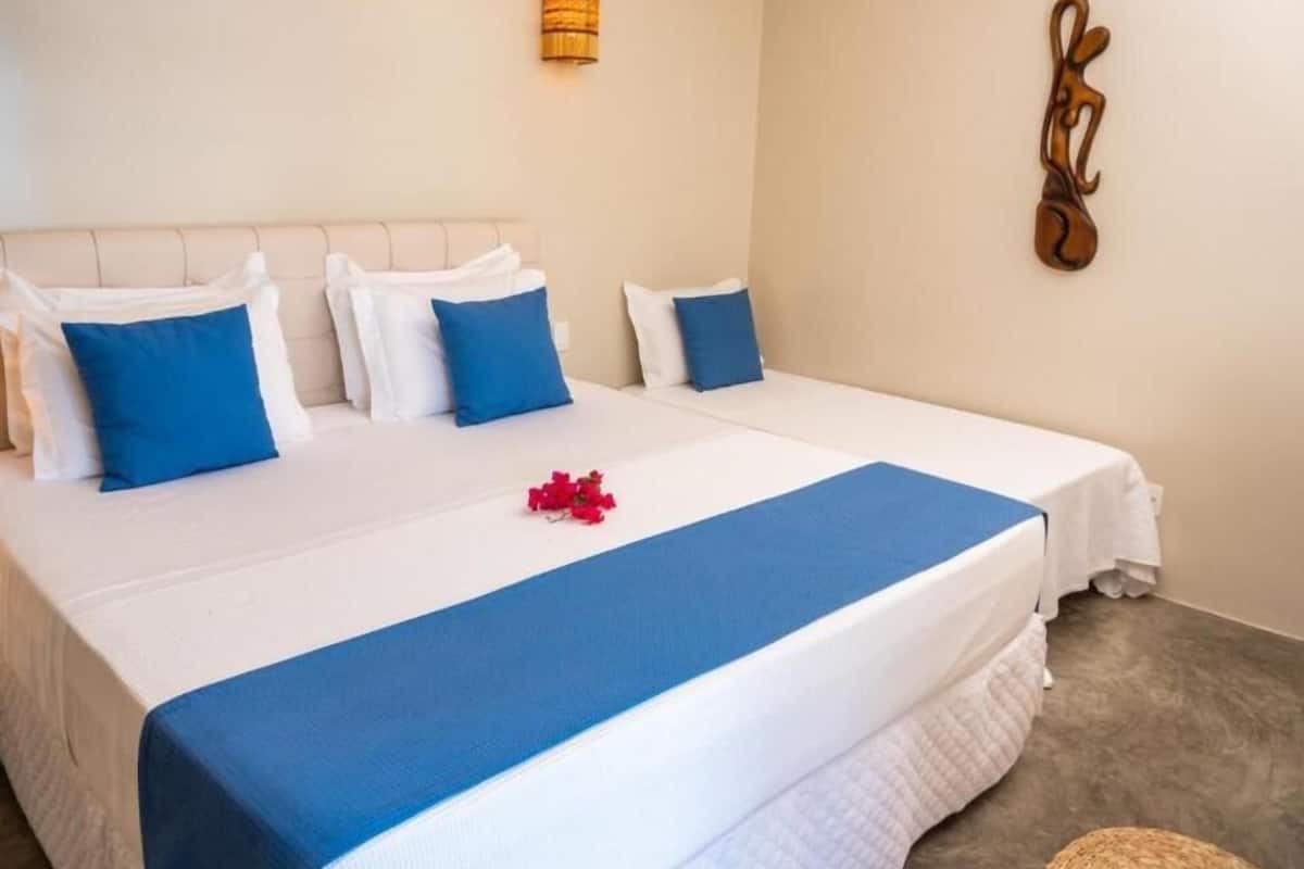 A neatly made bed with white and blue bedding, a decorative wall piece, and a small wall-mounted light fixture.