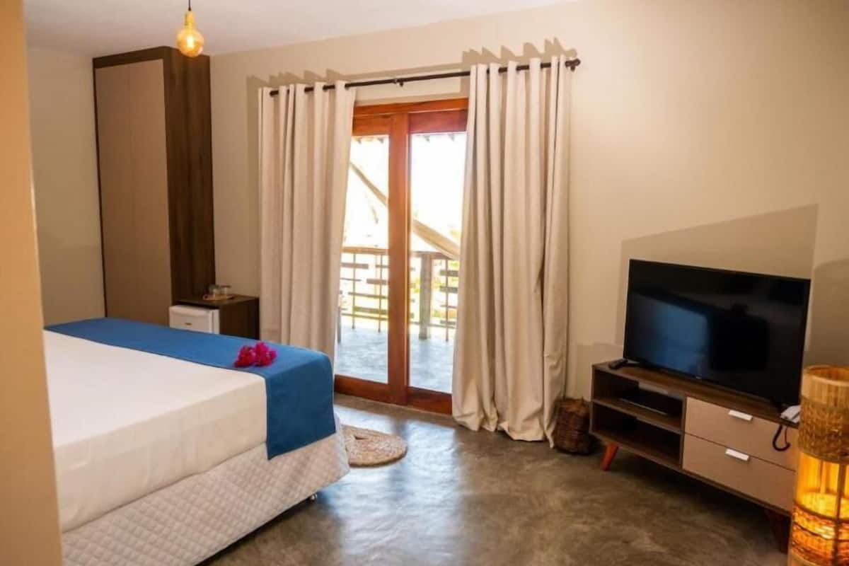 A bedroom with a bed, a television, a small table, and a window with curtains.