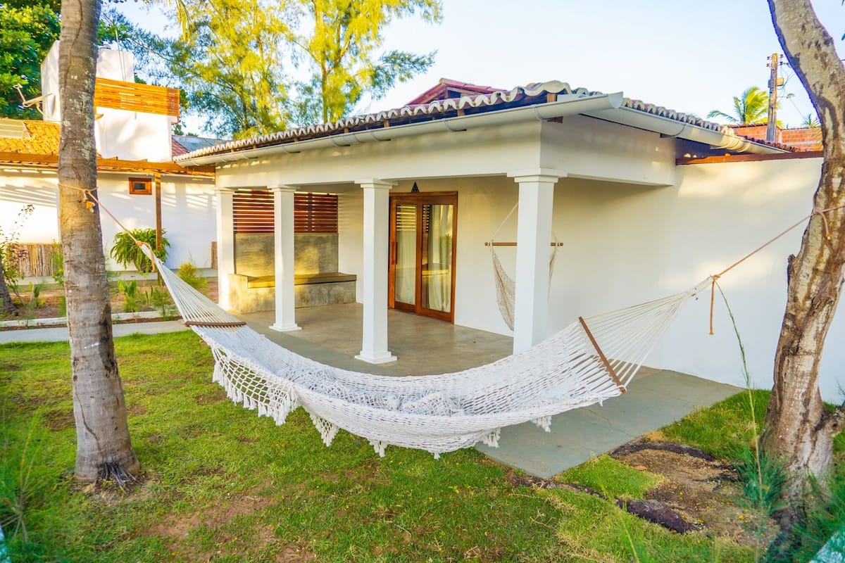 A white building with a covered porch, a hammock, and palm trees.