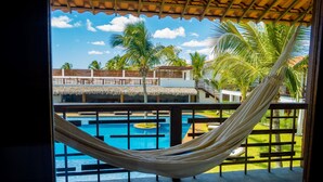 Una hamaca sobre una piscina con vistas a una zona de resort, que incluye una estructura de techo de paja y palmeras.