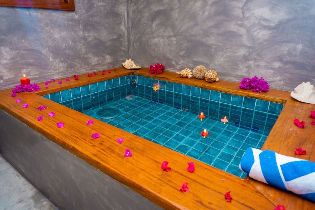 A rectangular hot tub with a wooden edge, surrounded by pink flower petals and candles.