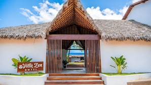 Hotel Villa Zen con entrada a techo de paja, una señalización y vista al océano.