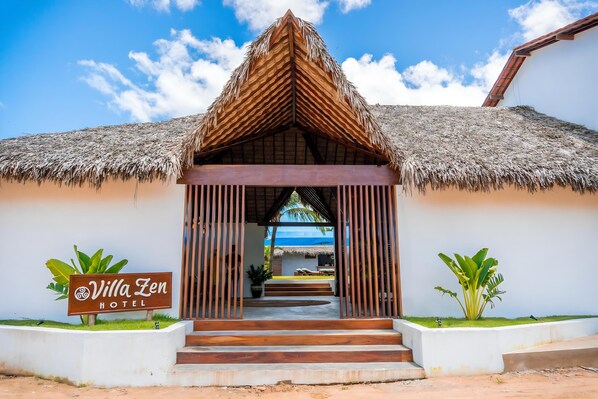 Hotel Villa Zen con entrada a techo de paja, una señalización y vista al océano.