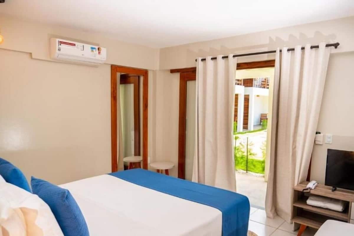 A hotel room with a bed, a small table, a TV, and a view of the outside.