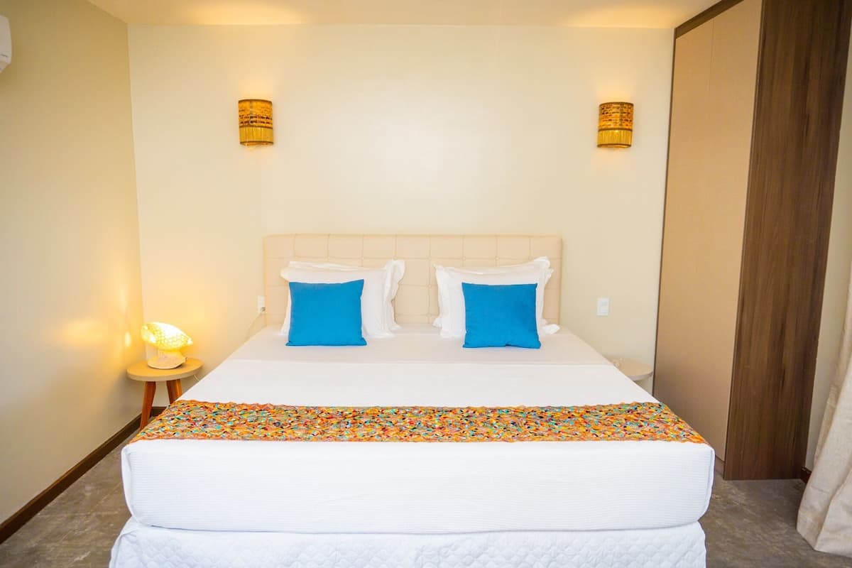 A hotel room with a bed, two blue pillows, a white bedspread, and two wall-mounted lamps.