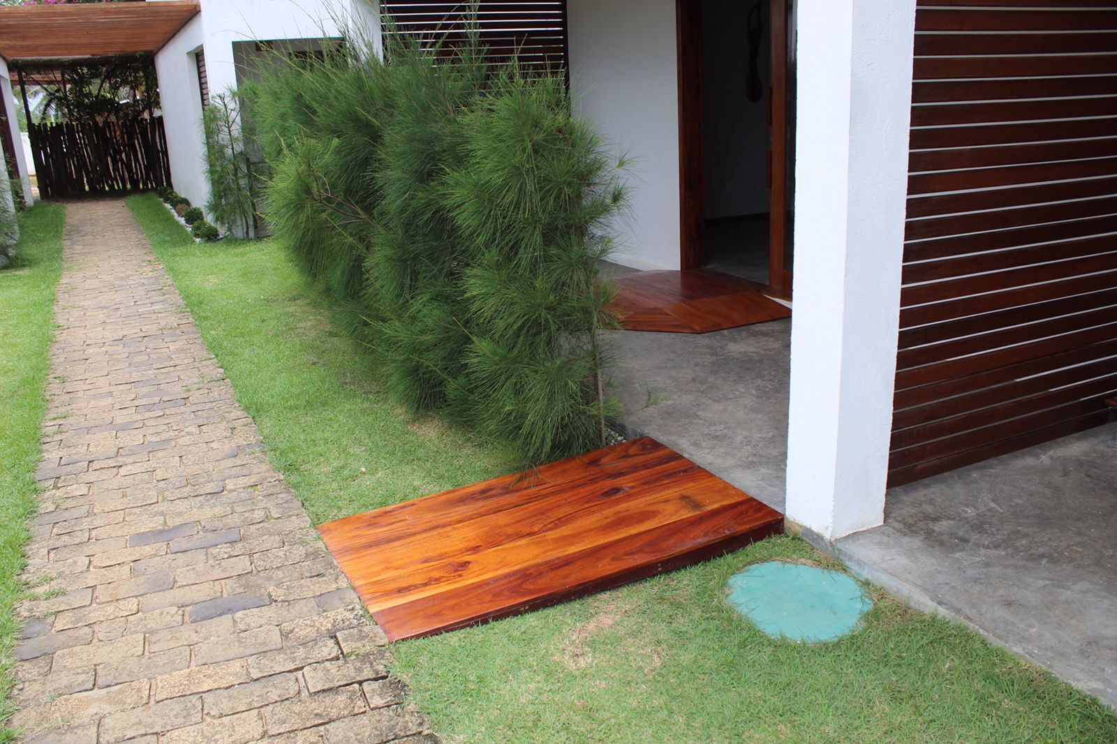 Un sendero conduce a una puerta de madera, rodeado de un césped cuidado y una valla de madera.