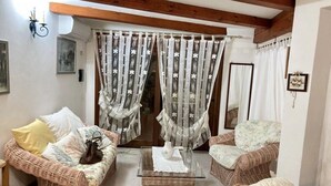 A cozy living room with wicker furniture, a glass coffee table, and floral curtains.