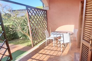 En balkong med ett bord och stolar, ett spaljerstaket och utsikt över grönska och en byggnad i bakgrunden.